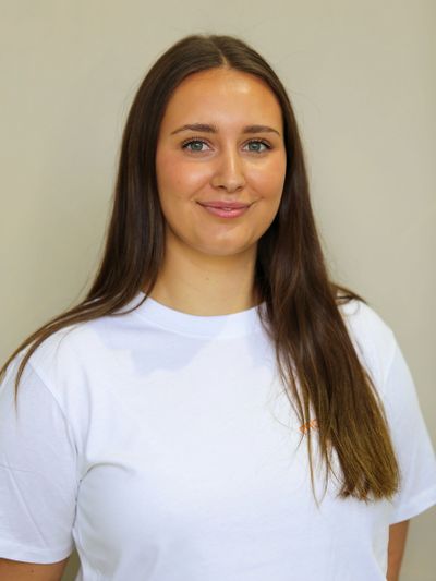 Young woman with long brown hair wearing a white t-shirt, smiling gently.