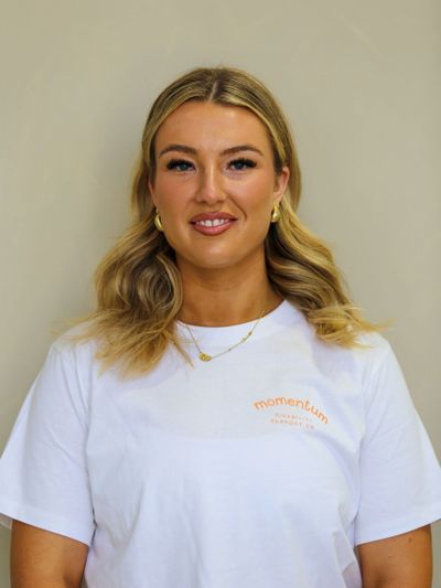 Smiling woman with blonde hair wearing gold hoop earrings and a white Momentum t-shirt.