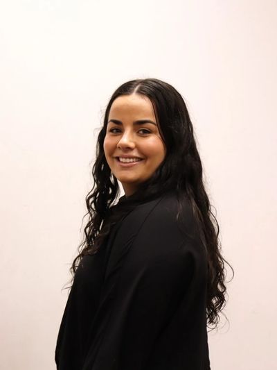 Smiling woman with long curly hair wearing a black top against a plain background.