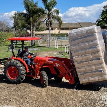 Our new 2025 Kubota tractor moving pallets of San Ynez shavings.