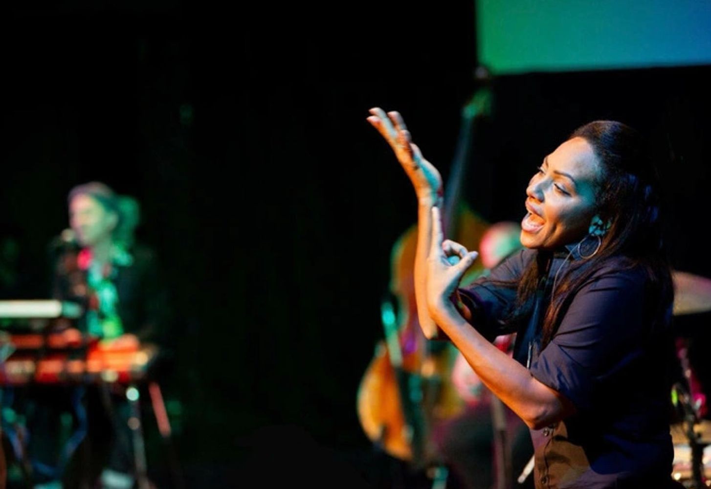 Mixed race interpreter on a stage performing a poetry piece in the foreground. Holding hands up.
