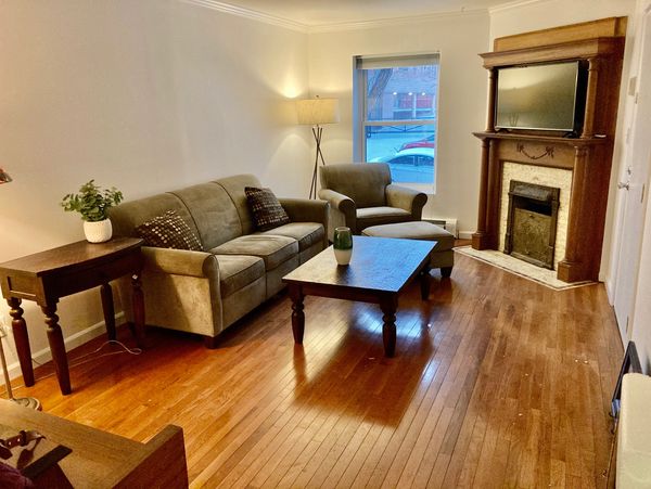 a living room with hardwood floors, a fireplace, and neutral furniture