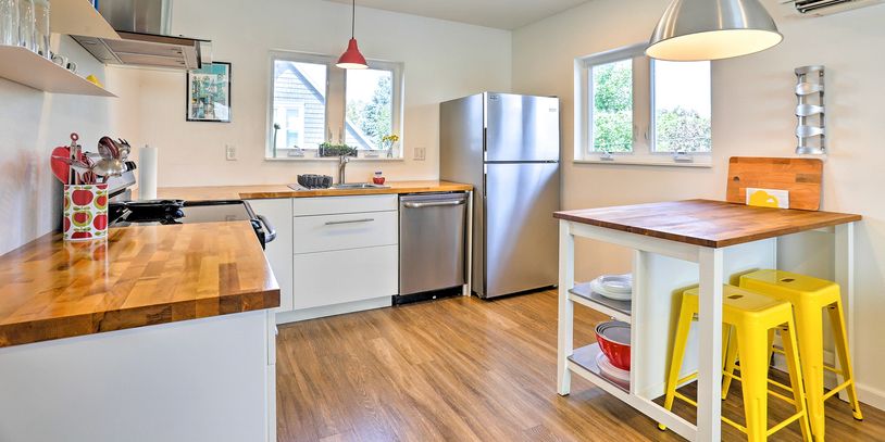 a bright, modern kitchen with stainless steel appliances, butcher block countertops,  yellow chairs