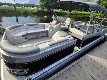 A luxury pontoon boat docked by the water with plush seating and a canopy.
