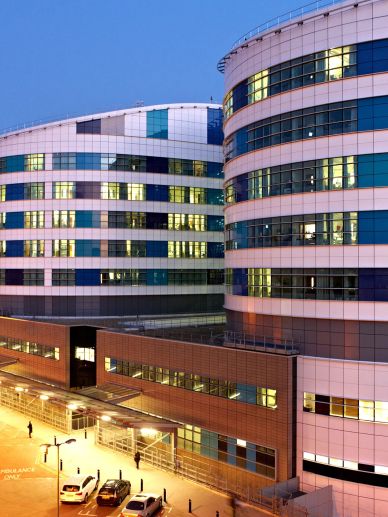 Modern hospital building at dusk with lights on.