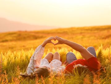 Couple making a heart shape with their hands lying in a field.