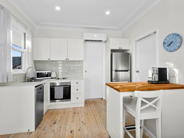 Bright white kitchen with wooden floor and modern appliances.