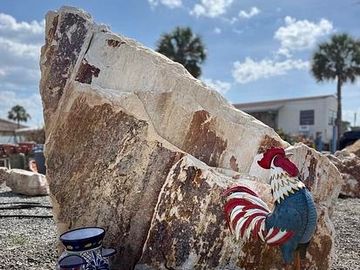Large marble stone with a rooster figure and vase nearby.