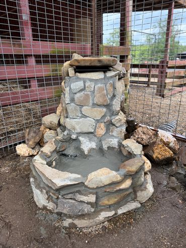 A newly built stone water fountain inside a fenced area.