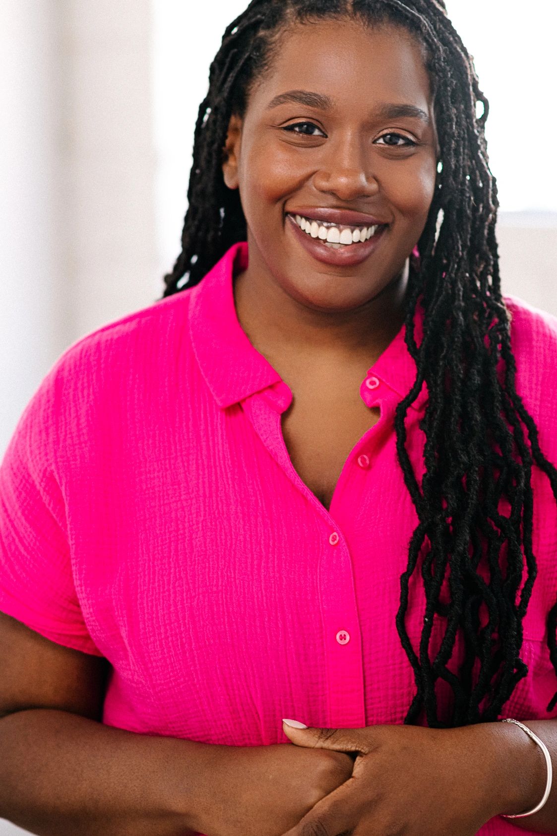 Smiling woman in a bright pink shirt with long braided hair.