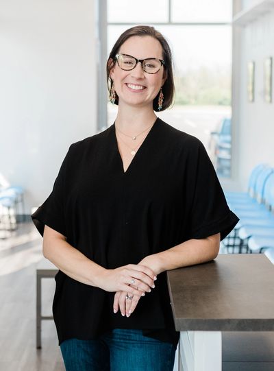 Smiling woman in glasses leaning on a counter in a bright room.