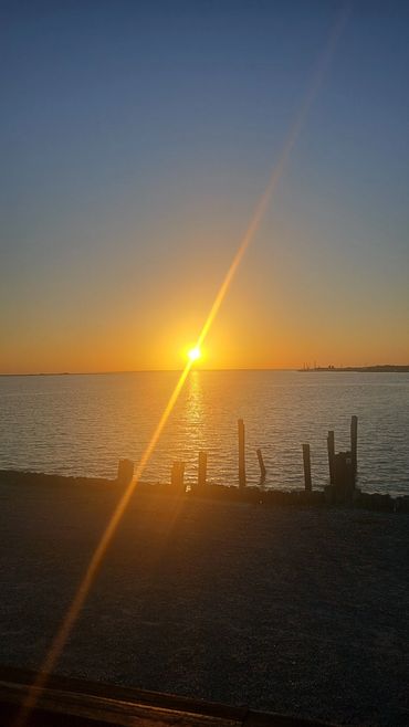 Sunset over calm water with silhouetted wooden posts at the shore.