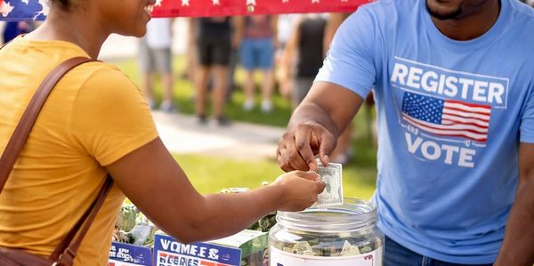 A person donates money at a voter registration event outdoors.