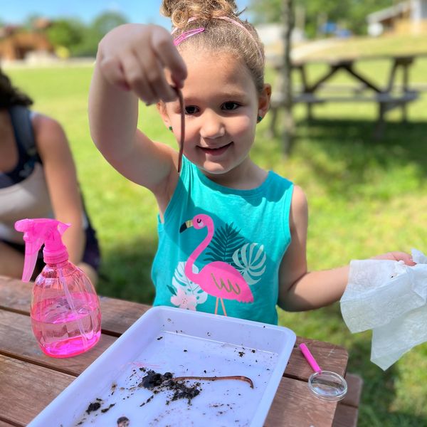 Girl holding an earthworm outdoors at a picnic table.