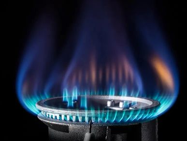 Blue flame burning on a gas stove burner against a dark background.
