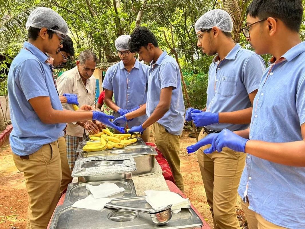 Young volunteers wearing gloves and hairnets serve bananas outdoors at a food distribution event.