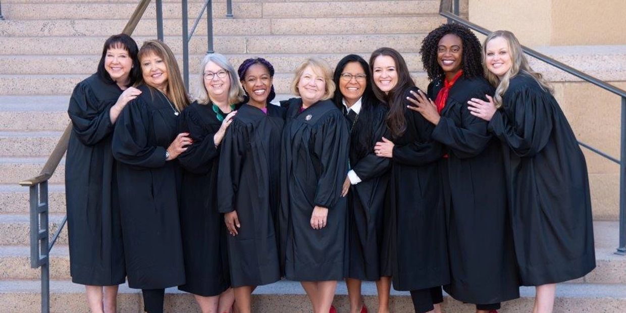 Group of women in black robes posing happily on stairs.