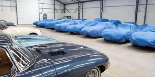 Classic cars in a garage, some covered with blue tarps.