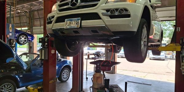 White Mercedes SUV lifted in a garage for repair.