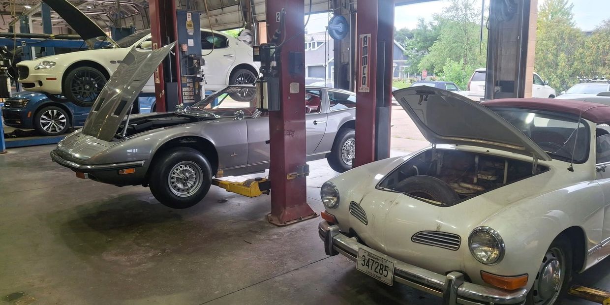 Classic cars in a garage with open hoods.