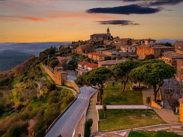 Sunset over a historic hilltop village with ancient stone buildings and lush greenery.