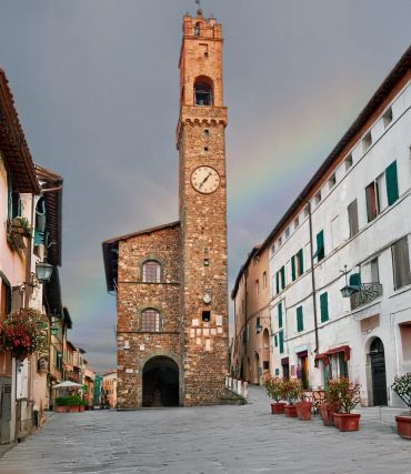 Historic clock tower in a quaint town square with a faint rainbow in the sky.