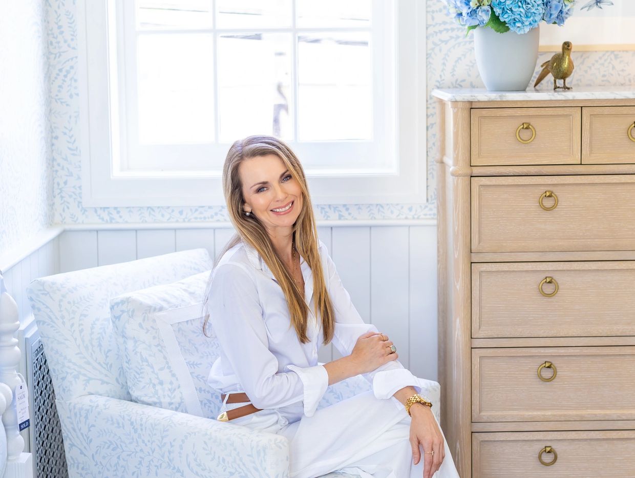 Smiling woman in white sitting on a patterned chair.