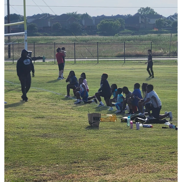 Children sitting on grass with coach nearby on a sports field.