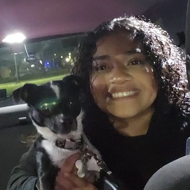 Smiling woman holding a black and white dog inside a car at night.