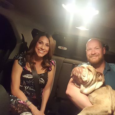 Couple smiling in a car with a bulldog on the man's lap.