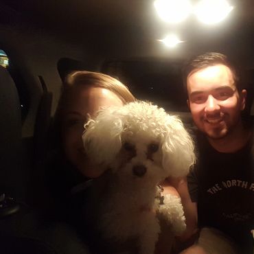 Two people and a white dog inside a car at night.
