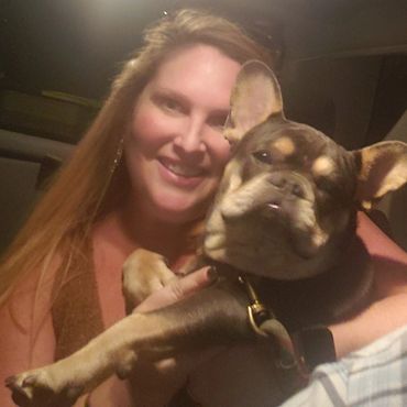 Woman smiling and holding a French Bulldog in a cozy indoor setting.