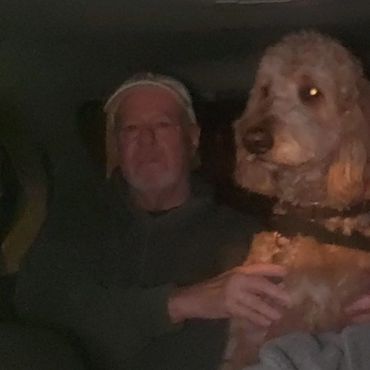 Man sitting in a dark room with a large dog on his lap.