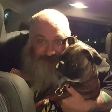 Bearded man holding a small dog inside a car at night.