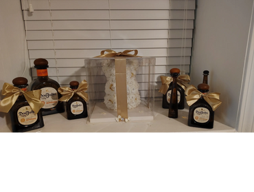 Don Julio tequila bottles decorated with golden bows around a white floral arrangement in a clear box.