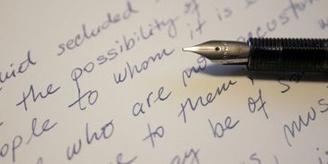 The image of handwriting on a piece of paper with a calligraphy pen laying on top of it.