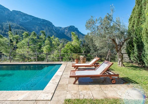 Sunny poolside with lounge chairs and mountain view.
