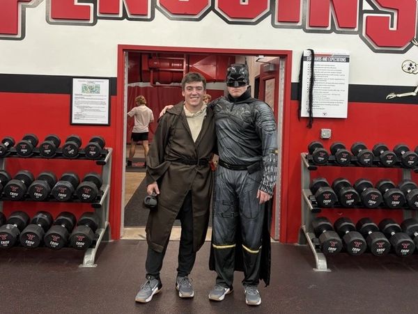 Two men in costumes at a gym posing for a photo.