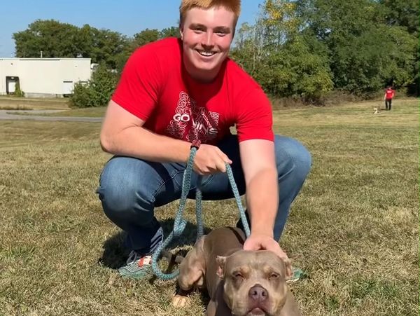 Young man smiling with a dog outdoors.