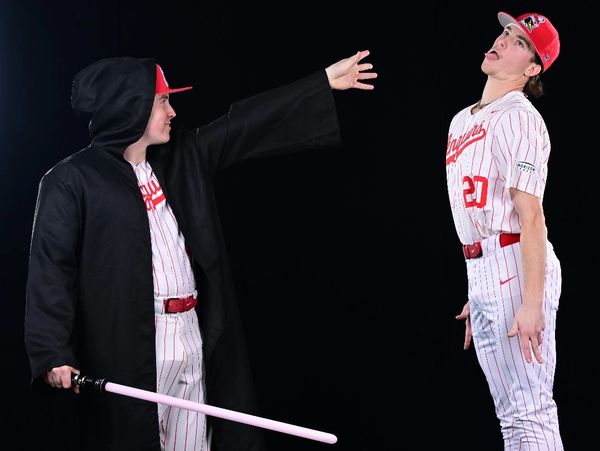 Two men in baseball uniforms, one dressed as a Sith using a lightsaber.