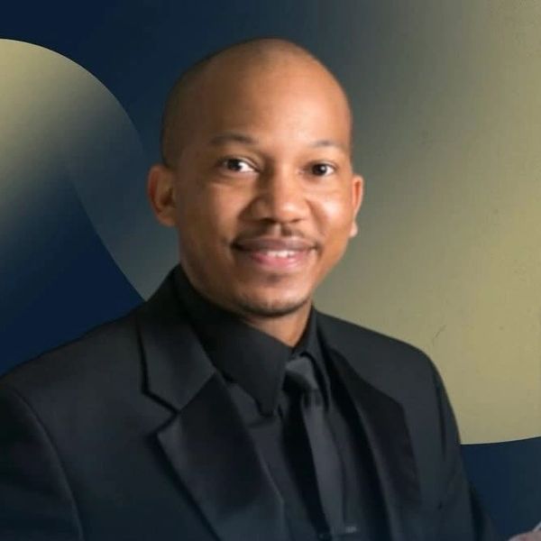 A man in a black suit and tie smiling at the camera.