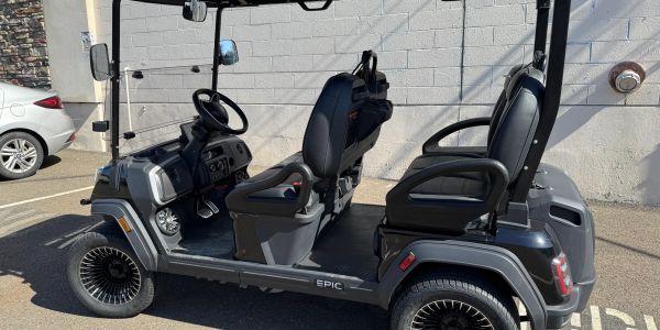 Black 4-seat golf cart parked by a wall in the sun.