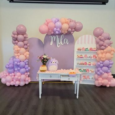Pastel balloon decorations with a table and cupcakes for Mila's celebration.