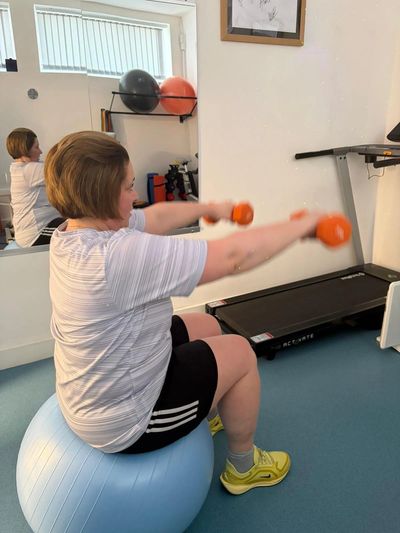 Woman exercising with dumbbells on a blue stability ball in a home gym.