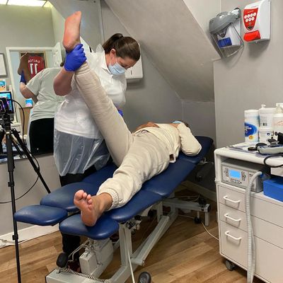 Physiotherapist stretches patient’s leg in treatment room.
