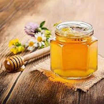 A jar of honey with honey dipper and flowers on wooden surface.