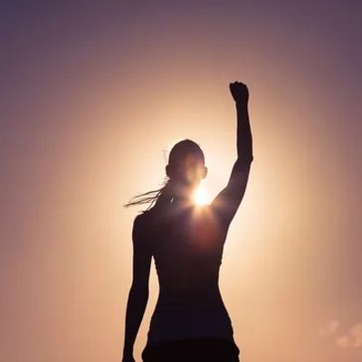 Silhouette of a woman against the sun in the background with arm raised in victory