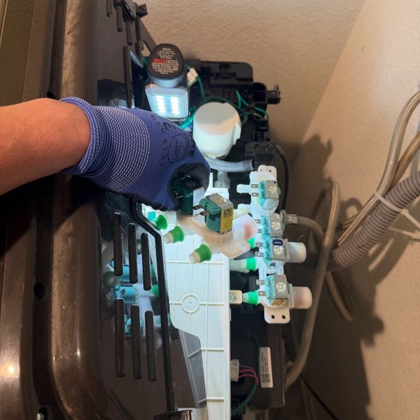 Hand with glove repairing washing machine valve assembly under bright light.