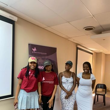 Four young women standing together in a room, smiling and posing for a photo.