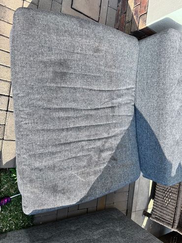 Gray outdoor cushioned seating on a stone patio under sunlight.